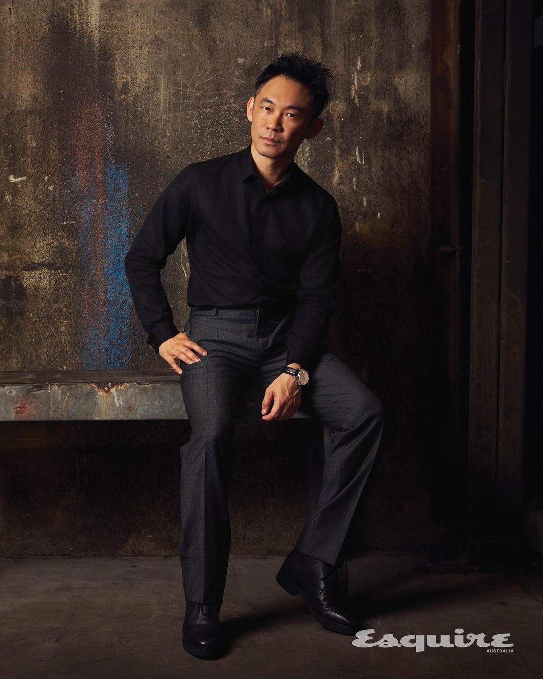 Portrait of a man in dark clothing sitting indoors against a textured wall with magazine logo in the lower right corner.