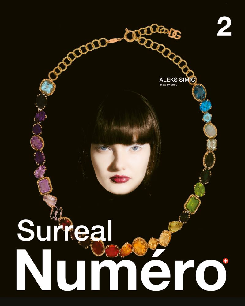 Close-up of a model surrounded by a large jeweled gold necklace against a solid black background for Numero Switzerland #2 March 2025 Covers.
