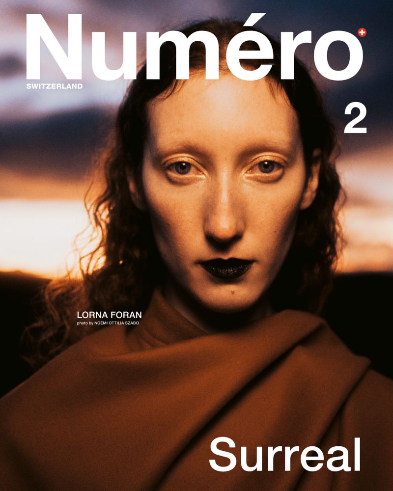 Magazine cover featuring a woman with dark lipstick and a brown shawl against a blurred sunset background with white sans-serif text.