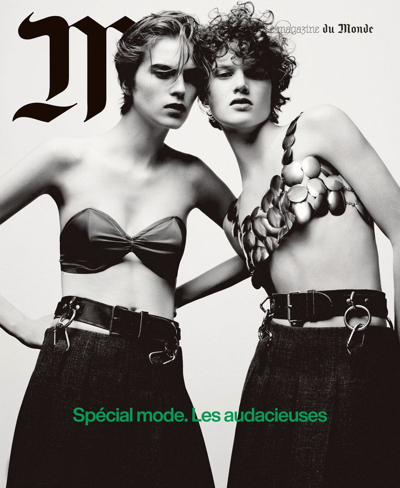 Magazine cover shot with two women posing in strapless tops and skirts with buckle belts against a light grey background.