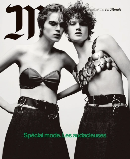 Magazine cover shot with two women posing in strapless tops and skirts with buckle belts against a light grey background.