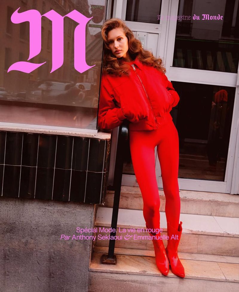 Magazine cover featuring a woman in a red outfit leaning against a building with pink logo on the window and magazine title at the top.
