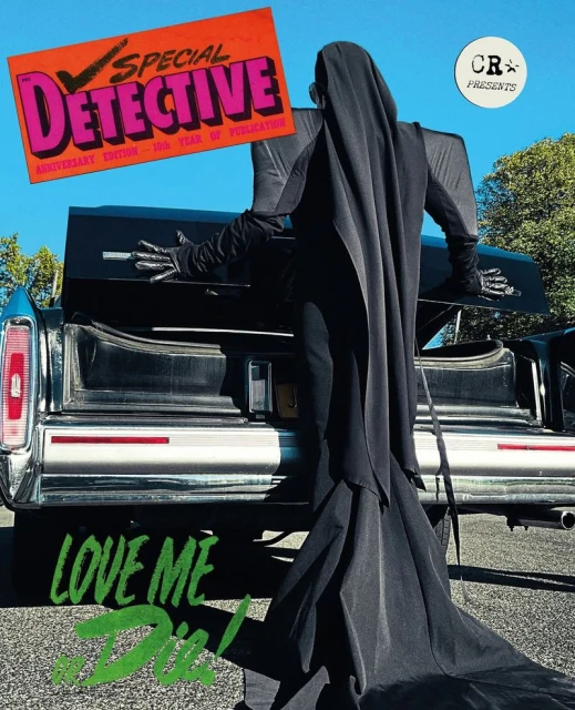 Figure in a long black hooded gown standing at the open trunk of a classic car against trees and a clear blue sky