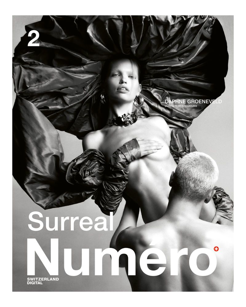 Black and white magazine cover featuring a topless female fashion model wearing an oversized fabric hat, with a male figure behind her.