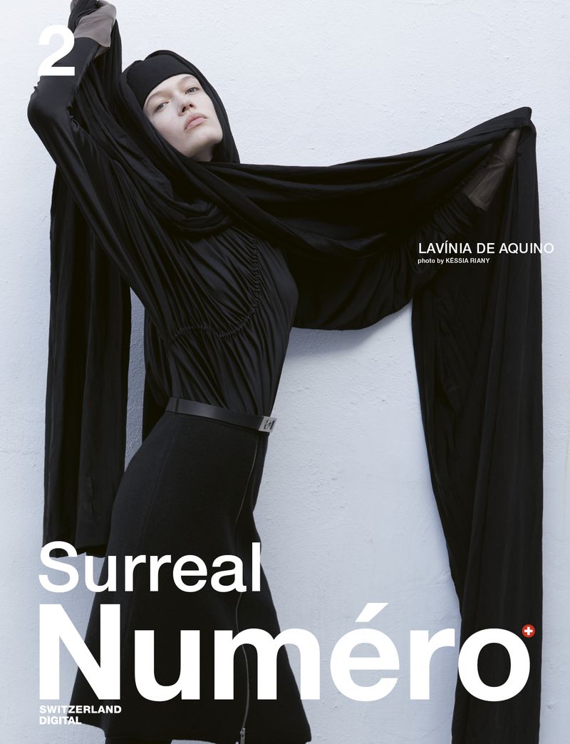 Model wearing a black dress and head covering holding out a long black fabric against a textured wall