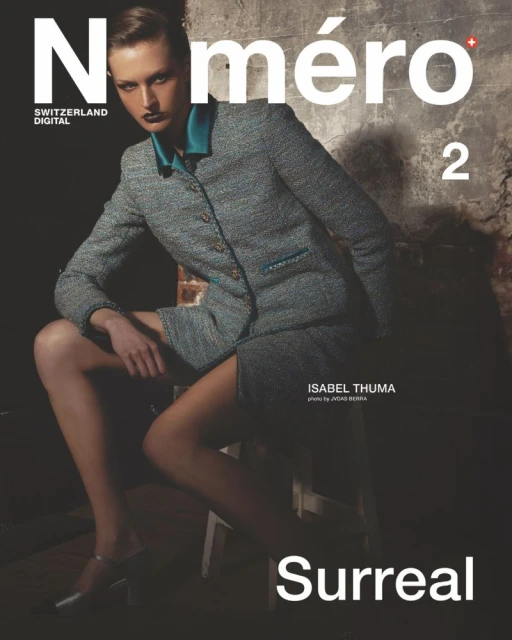 Fashion magazine cover featuring a model wearing a tweed suit, seated on a stool against a textured wall, with the magazine's title.