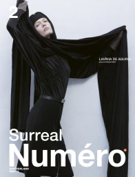 Model wearing a black dress and head covering holding out a long black fabric against a textured wall