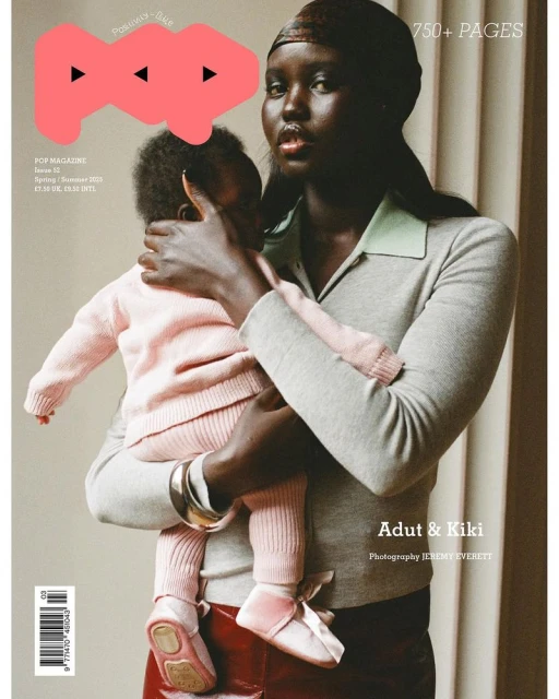 Magazine cover featuring a dark-skinned woman holding a child dressed in pink. The woman wears a grey sweater, standing against a neutral backdrop.