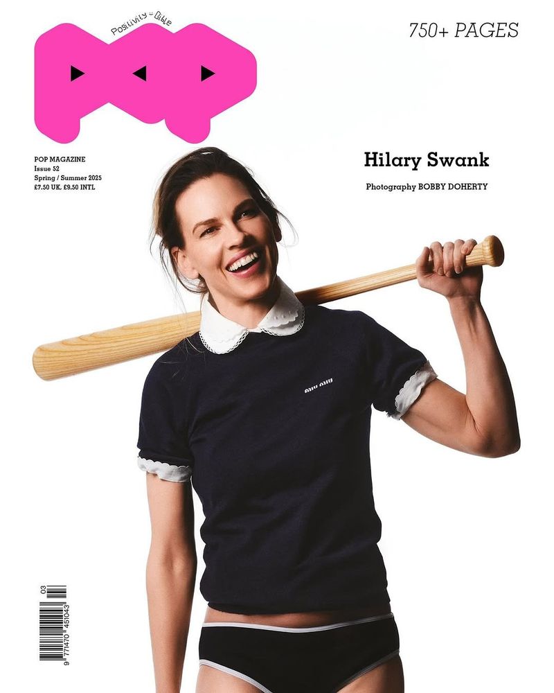 Magazine cover featuring Hilary Swank holding a baseball bat, set against a clean white backdrop with bold pink branding elements.