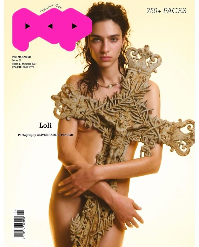 Fashion magazine cover featuring a woman posing nude holding a large stone cross, with the magazine's logo and text visible.