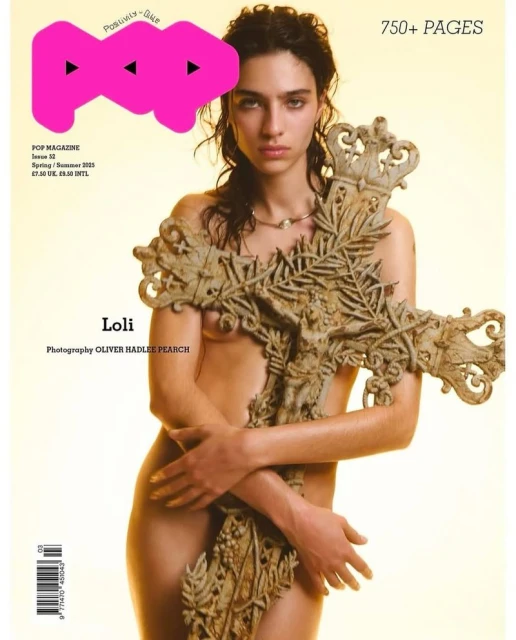 Fashion magazine cover featuring a woman posing nude holding a large stone cross, with the magazine's logo and text visible.