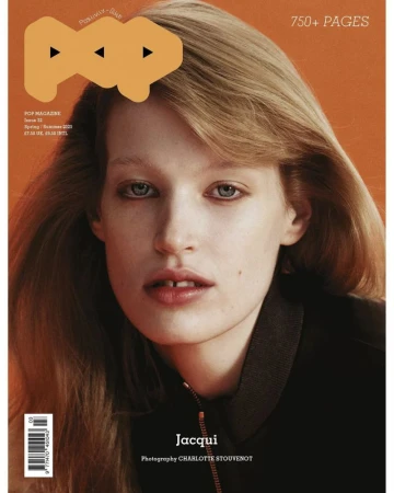 Close-up portrait of a woman with blonde hair wearing a black jacket against a solid orange background for Pop Magazine #52.