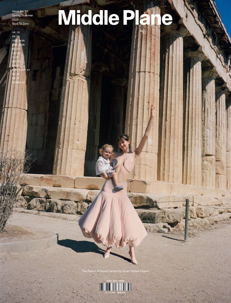 Magazine cover featuring an adult female holding a child in front of ancient Greek ruins under bright, natural lighting conditions.