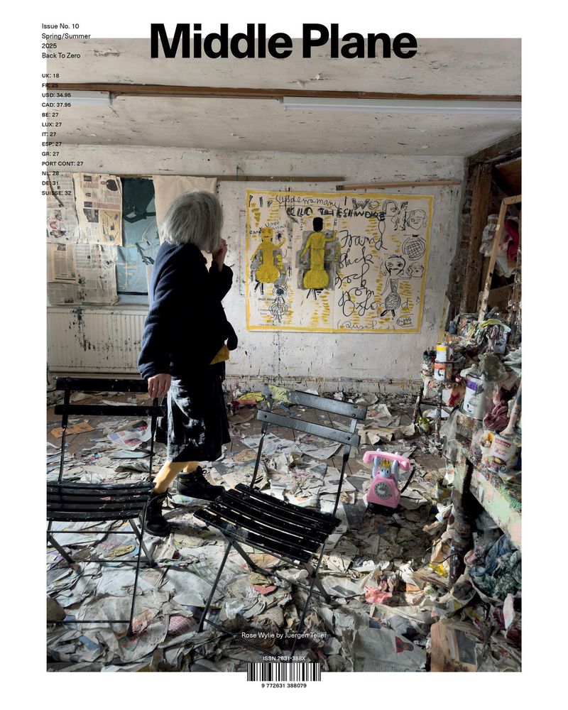 Magazine cover featuring a person in black jacket standing inside a cluttered, painted room with a pink telephone and chairs.