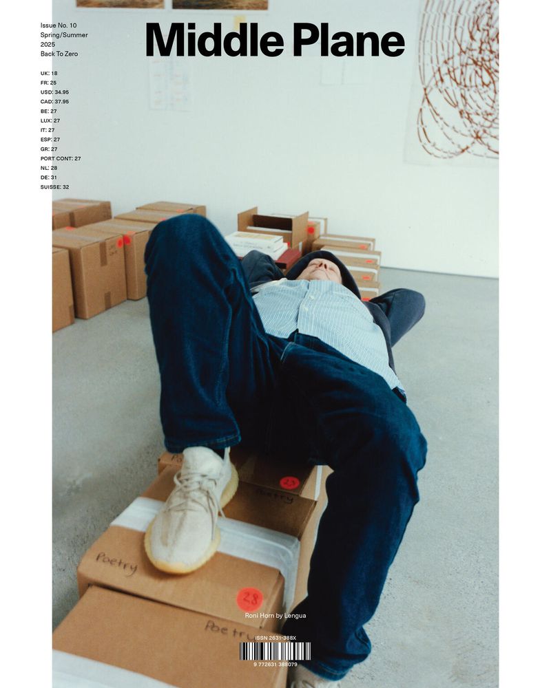 Man lies on cardboard boxes wearing jeans and sneakers inside a photo studio with modern art on white wall for fashion editorial.