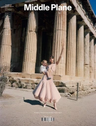 Model standing in front of classical stone temple columns holding a child in a pink skirt.