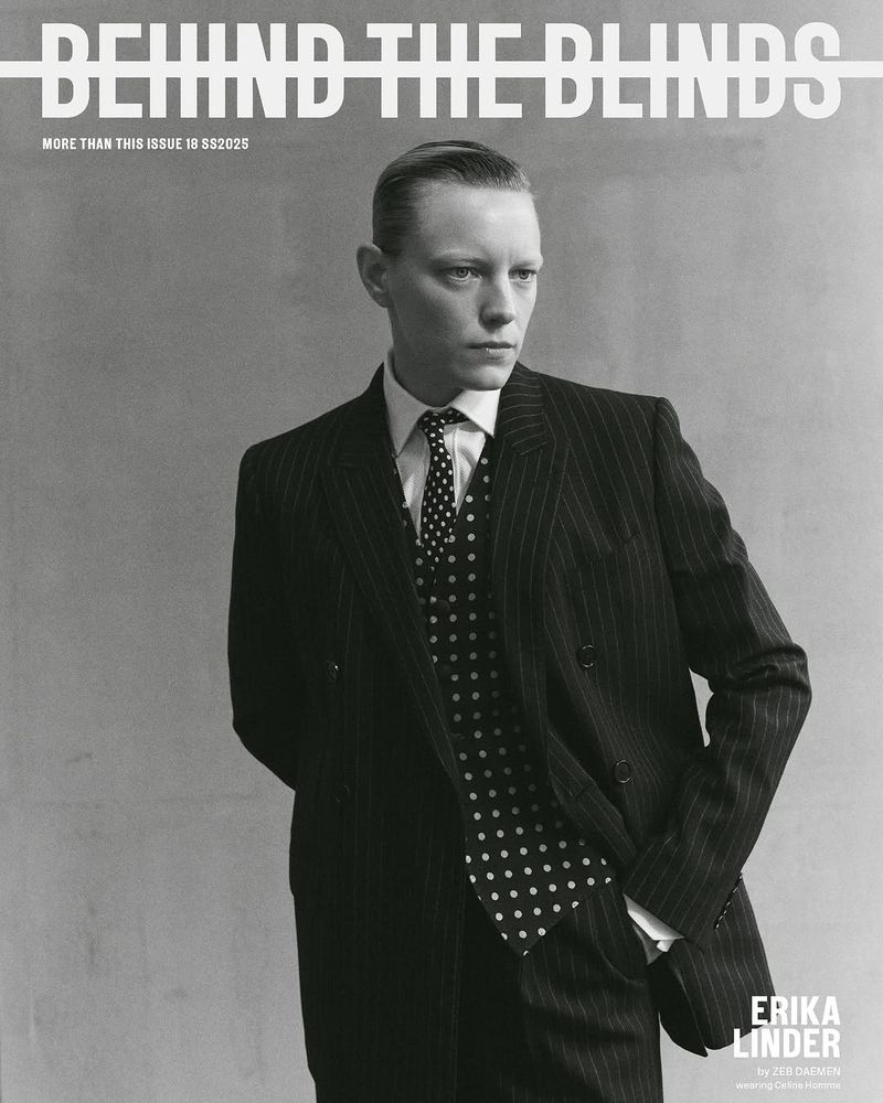 Black and white portrait of a person in a pinstripe suit with a polka dot tie against a grey background, magazine cover.