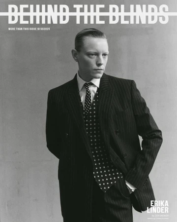 Black and white portrait of a person in a pinstripe suit with a polka dot tie against a grey background, magazine cover. 