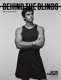 Antoni Porowski wearing a dark tank top and dark shorts with arms crossed against a plain grey background