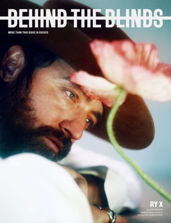 Close-up portrait of a man wearing a brown hat, looking past a large pink poppy flower held in the foreground.