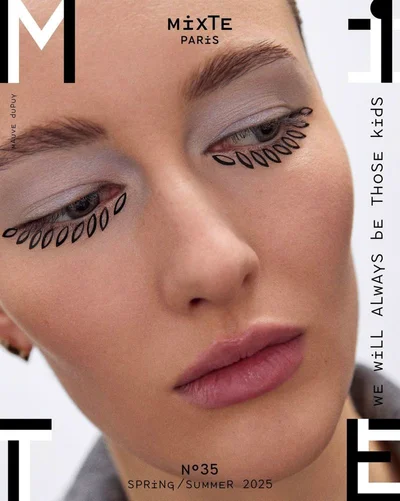 Extreme close-up portrait of a model with decorative eyeliner accents and soft purple eyeshadow against a white seamless background.