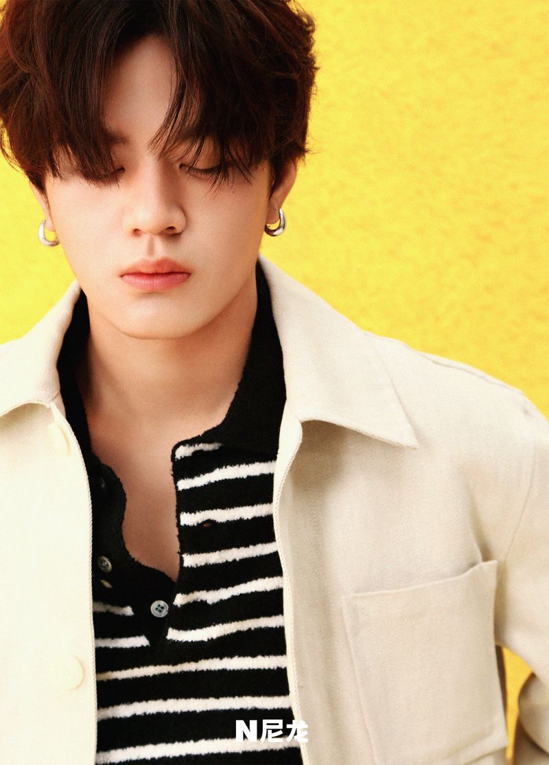 Close-up portrait of a young man with dark hair, closed eyes, and silver hoop earrings against a vibrant yellow textured background.