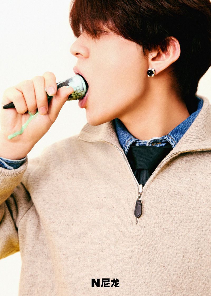 Young adult eats from a cone with green, black, and tan coloration in a studio shot featuring a beige zipper sweater.