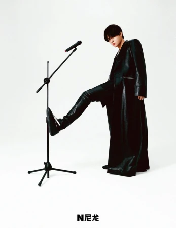 Person in black leather coat and boots stepping on microphone stand in studio. Stylish studio portrait on white backdrop.