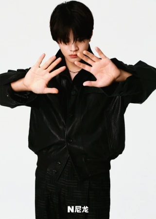 Young man in a black leather jacket holding up both hands towards the camera against a plain white background