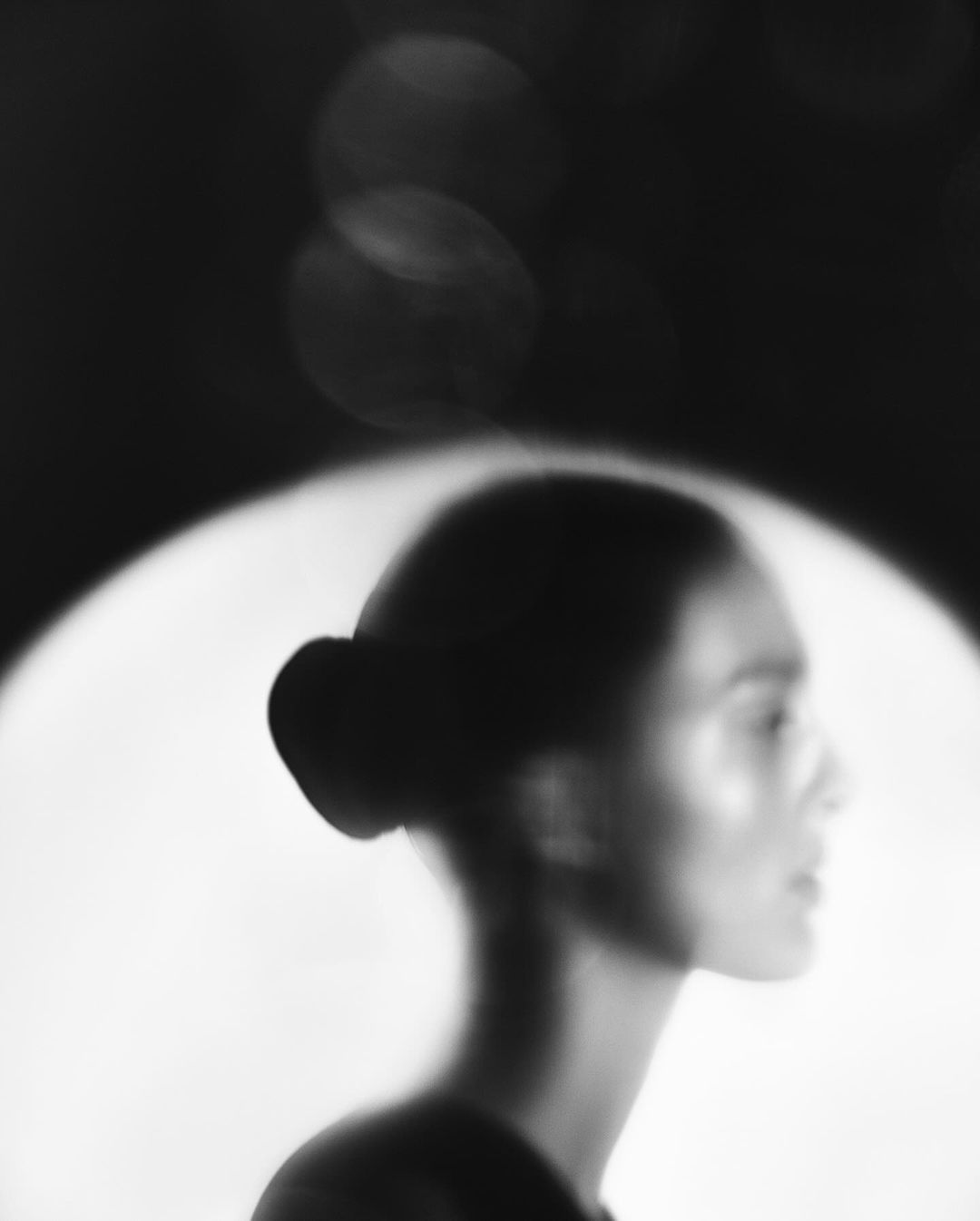 Monochrome portrait of a woman in profile with soft lighting, showcasing a shallow depth of field and a blurred background.