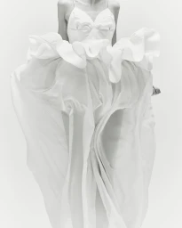 Model wearing a voluminous white dress with ruffled bodice against a plain white background