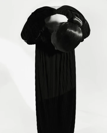 Model bowing forward in a long black dress with hair styled in a sleek updo against a white seamless background