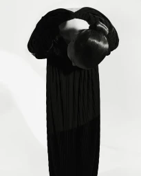 Model bowing forward in a long black dress with hair styled in a sleek updo against a white seamless background