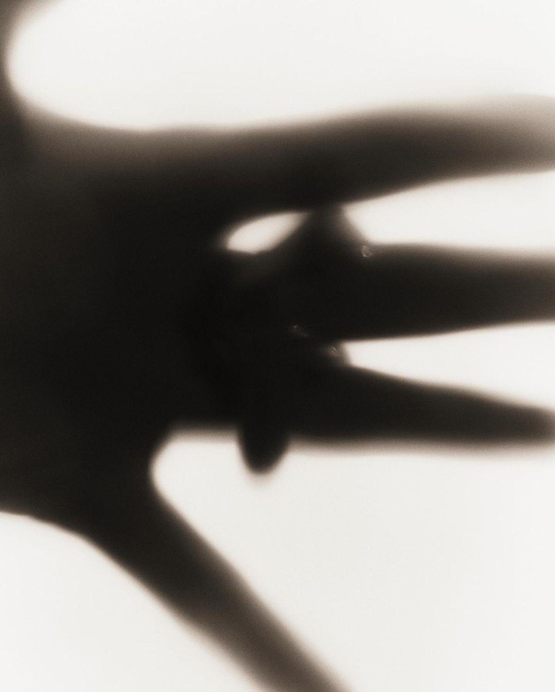 Close-up, high-contrast sepia photo of a human hand with outstretched fingers against a bright, blurred background, creating dramatic shadows.