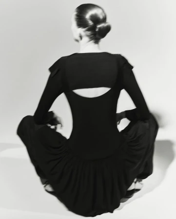 Model seen from behind wearing black top and trousers sitting against a light background
