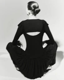 Model seen from behind wearing black top and trousers sitting against a light background