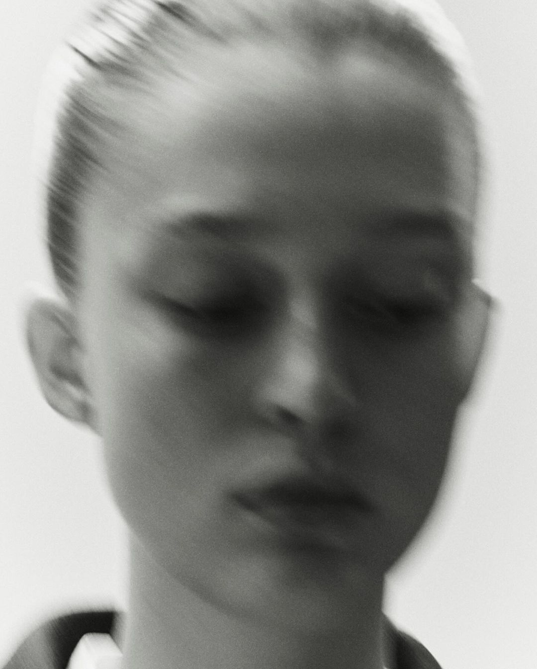 Close-up portrait of a model with hair tied back against a plain white background in a soft-focus motion style