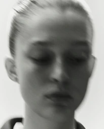 Close-up portrait of a model with hair tied back against a plain white background in a soft-focus motion style