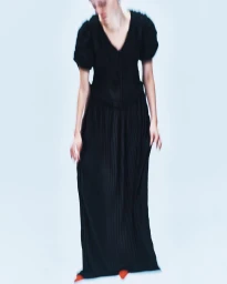 Model in a long black dress with puffed sleeves standing against a light background with motion blur