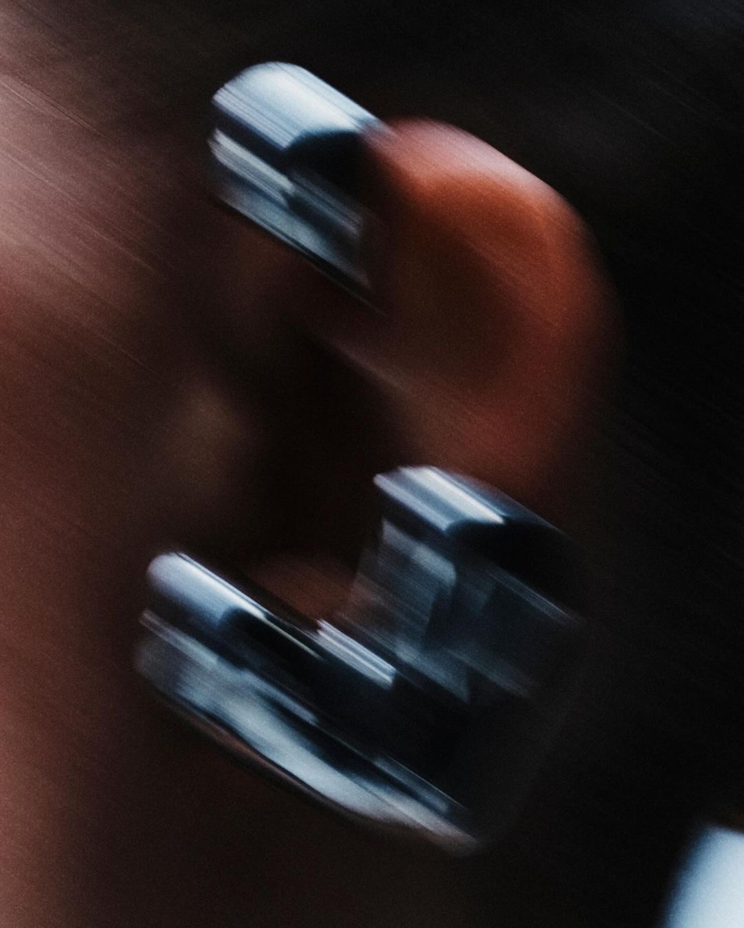 Close-up of hand with metal rings on fingers, featuring blurred motion and dark, moody color palette for an edgy aesthetic.