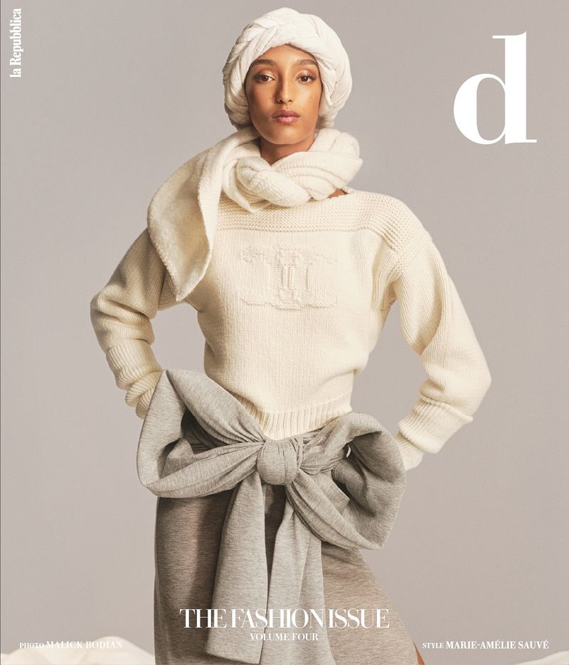 Fashion editorial featuring a woman in a cream sweater, scarf, and head covering, posing against a neutral background for a magazine cover.