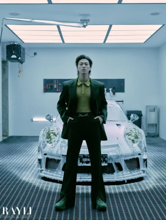 Man in dark suit poses in front of foamy Porsche inside garage with industrial lighting and tools in organized wall racks.