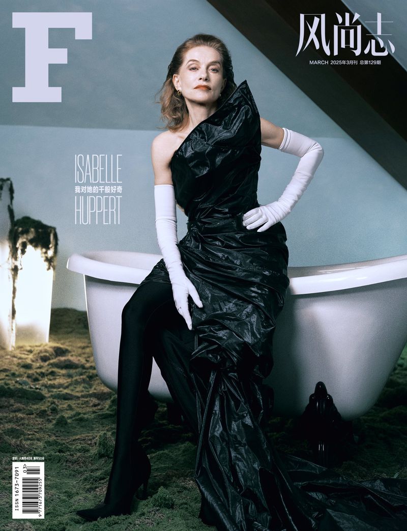 Isabelle Huppert on a magazine cover, posing in a dramatic black gown and long white gloves, sitting beside a white bathtub.
