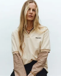 Model Emma Balfour wearing a cream polo shirt layered over a plaid undershirt against a white background