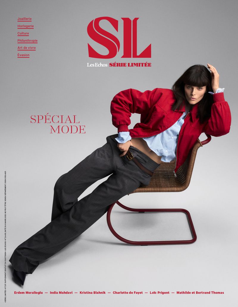 Fashion editorial featuring a woman in a red jacket and grey pants, leaning back on a woven chair with a magazine cover background.