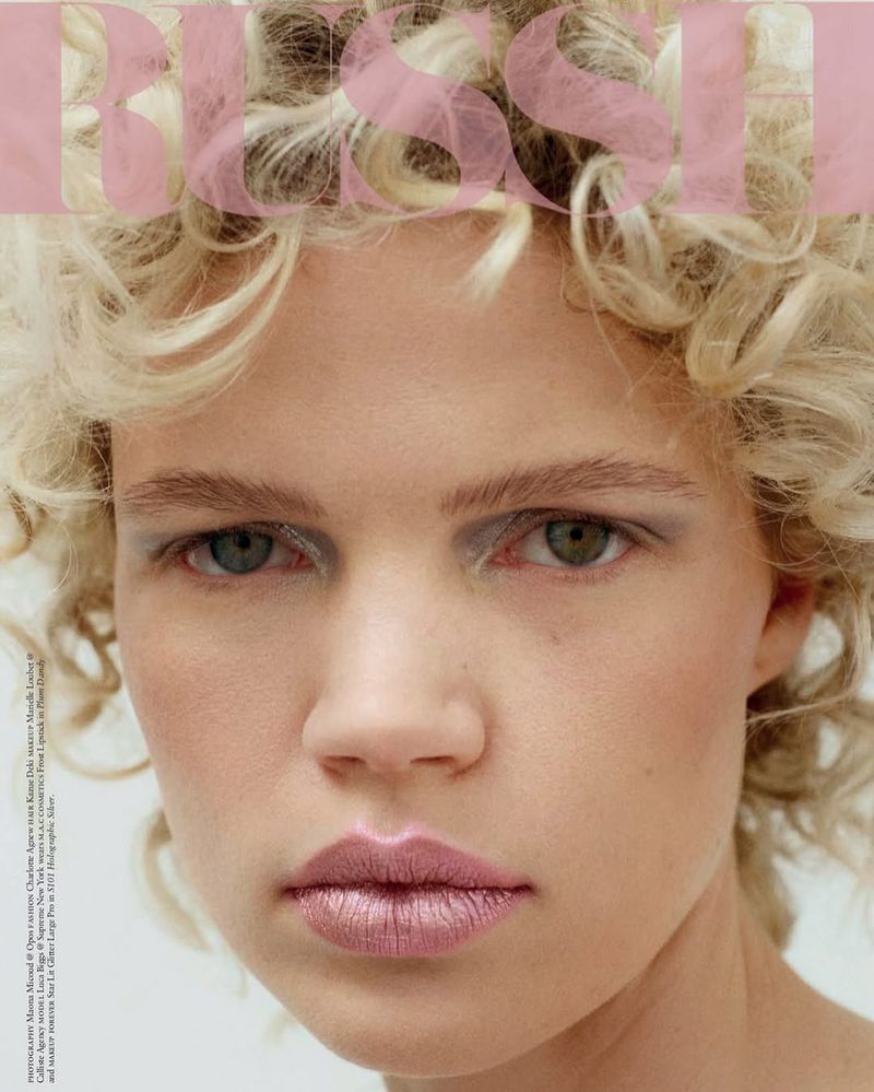 Close-up of a blonde woman with makeup looking at the camera. The word 'Bliss' is superimposed on the image in pink text.