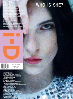 Close-up portrait of a dark-haired woman with pale skin and light eyes on a magazine cover with pink logo branding.