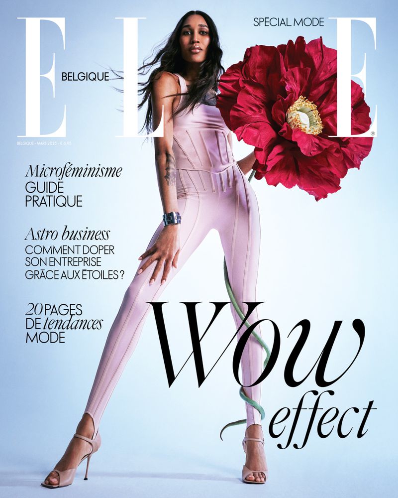 Magazine cover featuring a slender adult female model in a fitted pink jumpsuit, holding a large red flower on a light blue background.