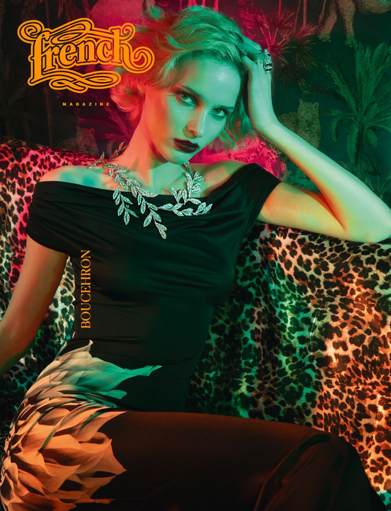 Fashion magazine cover featuring a blonde model wearing a black top and floral pants, posing on a leopard-print sofa, with green and orange lighting.