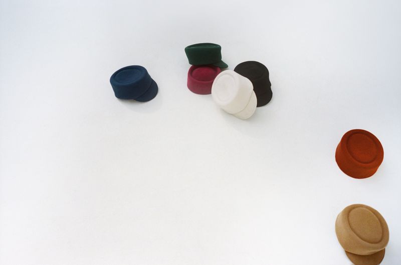 Collection of colorful pillbox hats arranged on a white surface, showcasing different shades including blue, green, red, white, and brown.